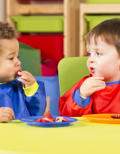 A stock photo of toddlers eating fruit and having a chat in the playroom.